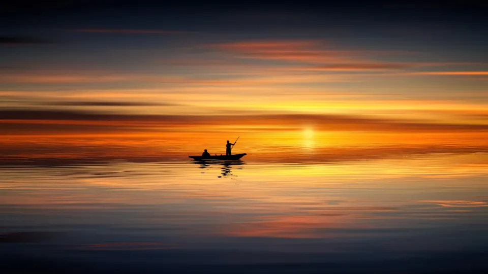 Small fishing boat silhouetted on calm water at sunset